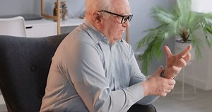 Retired old senior man, elderly person alone at home, suffering from arthritis and holding, rubbing his painful hand. Feeling bad problems with joints, fingers, wrist pain, rheumatoid inflammation