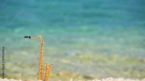 Mini model of real alt tenor saxophone stands white small pebbles on seashore, against background of blue turquoise water. Music screensaver for romance. Slow motion video. Copy space for your text.