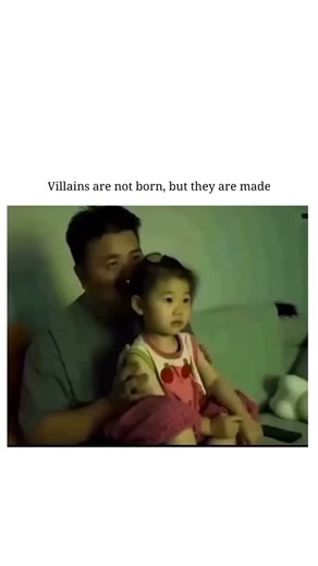 world memes.io on Instagram: "The scene is set in a home environment, likely a living room. A man is sitting on a couch with a young girl (around 3–4 years old) on his lap. Both are looking toward the camera/TV. The Setup: The video begins with a somber, cinematic music track and the caption: "Villains are not born, but they are made." This sets up a dramatic expectation for the viewer. The Action: The father reaches around and uses his hands to pull the skin around the girl's eyes and mouth upw