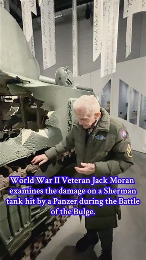 WW II Veteran Jack Moran examines damage on a Sherman tank hit during the Battle of the Bulge.