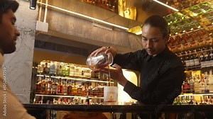 Bartender presenting classical in Old fashioned whiskey cocktail pouring into cooling glass recommending special welcome tasty creative drink with smart VIP guest at luxurious beverage bar. Vinosity.