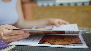 Woman reading restaurant menu close-up. Female hands holding menu in cafe turning pages choosing food and drinks. Picking refreshers and beverages. Selecting. Slow motion