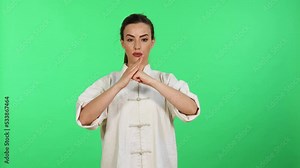 Young caucasian woman in white kungfu wushu uniform practicing martial arts and salutation while looking in camera. Green screen for chroma key in background