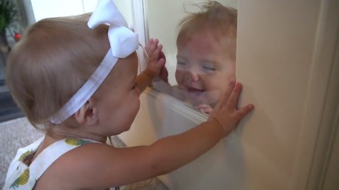 The twin baby girls laugh adorably through the glass