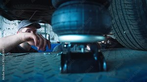 Two mechanics collaborate on vehicle maintenance, using specialized tools under the lifted car in a busy automotive workshop.