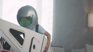 Childhood, teen boy in an astronaut costume plays with a cardboard space shuttle, runs around the room.