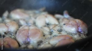 Traditional cooking of fried frog legs on pan.