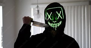 A scary slasher serial killer in a horror halloween mask pulling a knife on his murder victim.