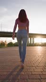 Vertical Video, Rear View of a Slender Woman in Jeans Walking through...