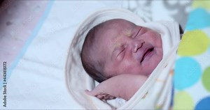 Upset Asian newborn baby girl starts to wake up and cry then fell asleep again when mother rocking crib. Adorable 0–6-month-old infant with closed eyes. Neonatal care for first days of life concept.