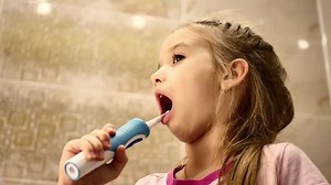Beautiful young girl brushes teeth by electric brush, smiling, drops out milk teeth, concept of health.