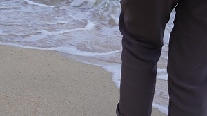 View of back close up legs of young beautiful woman. Walking barefoot on sand on beach by sea.