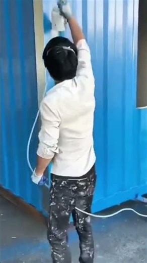 spraying bright blue paint on metal shipping container walls using professional electric air gun