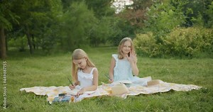 two girls with long hair they do homework and draw in a notebook in a green park