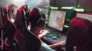 Young gamer plays a video game, side view, uses gaming mouse and keyboard, illuminated coral color and multicolor neon, cybersportsman.