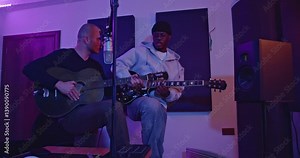 Two musicians create music together, playing guitars and recording in a professional studio.