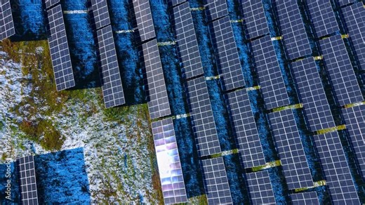 Solar panels in winter field with sun reflection. Close up aerial view of solar modules with bright sun glare reflecting off one panel surface during winter.