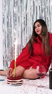 cheerful woman wearing red dress celebrating birthday and lighting sparkler candles on red velvet cake