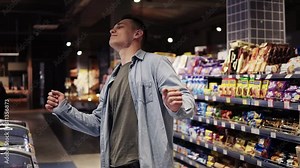 At the supermarket: Happy stylish man with dances freerly in big shopping mall in front the shelves with goods. Positive dances in an empty food store