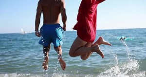 Bare feet of man and woman jump in air on beach in sea