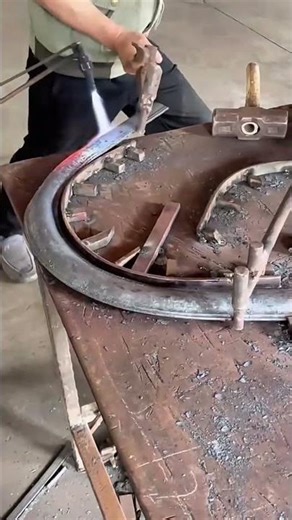 heating metal using a torch and hammering it into a curved shape on a professional workshop table
