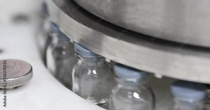 powder injection vaccine medical drug filled glass vials moving and rotating and being capped in an injection production line in a pharmaceutical manufacturing company