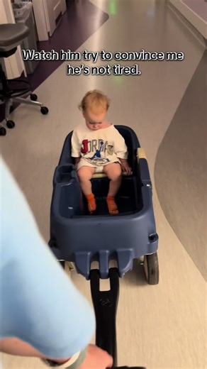 Three days in the hospital… THREE. * And on the LAST day my man decided sleep was no longer part of his personality. * Sir. You have had nurses in and out. Monitors beeping. People poking you. But NOW you’re energized?? * He said he wasn’t tired. The wagon said: “bet.” * I put him in it to roll the halls one last time before discharge and within two minutes he was blinking in slow motion like Windows 95 shutting down. * Fighting sleep like it owed him money. The hospital couldn’t take him out… b