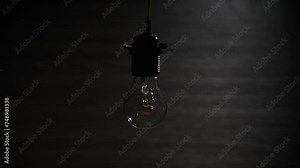 Hanging on wire incandescent bulb turns on, and off and flickers on black background, place for text. Warm flashing filament close-up. Glass old bulb glowing yellow warm light. Tungsten lamp. Idea 4K
