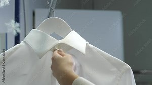 Close-up of shirt hanging in process of steaming while female hand holding it on during professional dry-cleaning in salon. Skillful woman employee cleaning clothes using steamer to remove dirt