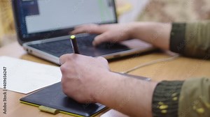 Side view of man draws and works at a computer using a graphics tablet