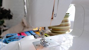 Woman hand close up sews tulle on electric sewing machine. Filling the thread into the sewing needle, adjusting the tension. Comfort in the house, a housewife's hobby, layout of sewing tools