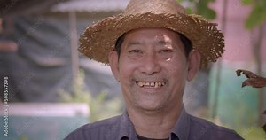 Happy smiling Asian male farmer with long teeth wearing woven leaf hat who grows ornamental plants in pots for market.