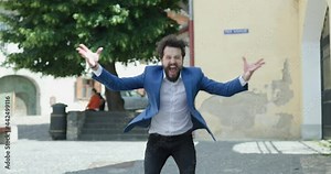 enthusiastic smart casual man getting good news, screaming, holding arms up in the air, gesturing and cheering the victory by dancing in front of medieval city background outdoor