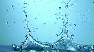 A closeup shot of a water drop splashing on a transparent glass surface, creating a mesmerizing electric blue effect against the sky backdrop