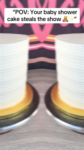 This luxury two-tier teddy bear baby shower cake is the perfect statement piece for welcoming a baby boy. Designed with smooth and textured white buttercream, this cake features a cascading balloon-style accent in soft blues, browns, neutrals, and metallic gold. Adorable teddy bear details wrap each tier, adding charm and warmth, while the elegant gold script topper gives a high-end, custom finish. Perfect for baby showers, sip-and-sees, and first celebrations, this cake blends classic teddy bea