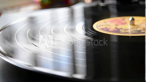 Spinning vinyl record on turntable creates light reflections. Spinning vinyl record presents a retro aesthetic with shifting arcs and circular motion, reflecting light in a dynamic way.