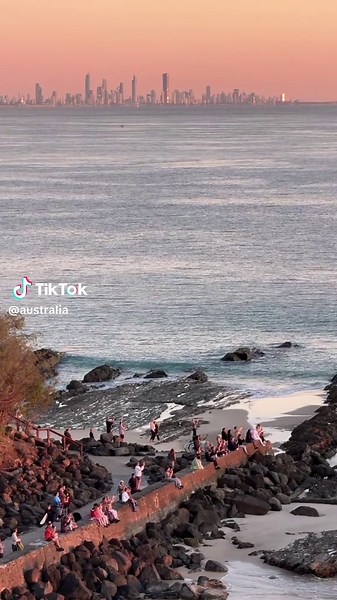 Sit back, relax and watch the sun rise over the Gold Coast ☀️ 🎥: IG/stillsbysav 📍: @Experience Gold Coast, @Queensland, Australia #SeeAustralia #ComeAndSayGday #ThisIsQueensland #ExperienceGoldCoast ID: People gathered by the ocean on a headland, watching the sunrise with a city skyline in the distance across the water.