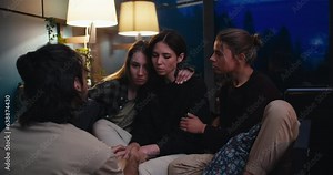 Three girls and a guy communicate in the evening in a cozy room. A sad girl talks about her experiences, and her friends support her