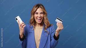 Young woman wear classic suit jacket beige t-shirt use mobile cell phone app hold in hand credit bank card do online shopping order delivery to home isolated on plain dark royal navy blue background Stock Video