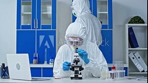scientist giving sample to coworker near microscope and laptop