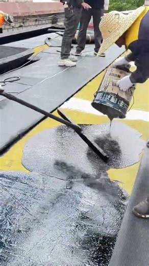 Saturating unfinished cement floor while evenly spreading black adhesive across the entire surface