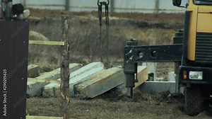 Piles are laying on the ground and ready for use by old tracked driver with hammer. Real estate market. Construction of residential buildings.