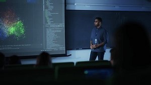 Portrait of a Young Male Teacher Giving a Data Science Lecture to Diverse Multiethnic Group of Female and Male Students in Dark College Room. Projecting Slideshow with a Neural Network Model