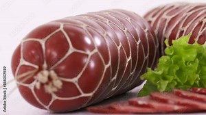 Dolly: Processed meat products sliced. Smoked sausage servelat in a netting on white background. Sausage cut with slices and herbs closeup.