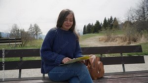 Woman sitting on wooden bench with paper map. Tourist looking for destination location on paper map, pointing at places and looking around. Close up. Front view