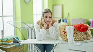 Young blonde woman leaning on ironing table with sad expression at laundry room Stock Video
