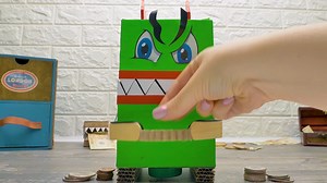 Una alcancía COME MONEDAS de cartón Slime Sam tiene un sueño. Quiere comprar una COSA. Así que está ahorrando dinero. El problema es que olvida dónde dejó las monedas. Su amiga humana, Sue, encuentra las monedas sin problemas. ¿Será porque Sam usó los zapatos de ella como escondites para las monedas? Sue tiene una mejor idea para una alcancía. ¡Va a crear una alcancía automática! Tú también puedes hacerlo. Pero asegúrate de pedir ayuda a un adulto con el motor. Esta alcancía consiste en dos part