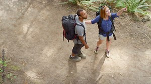The camera looks down on a couple who are hiking in the forest but then stop to take a picture