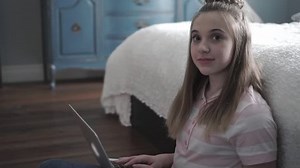 A Young smiling teen girl on bed with laptop