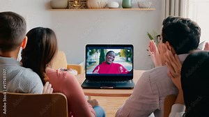 A group of family members gathers around a laptop, engaging with a lively host on-screen while sharing smiles and laughter in their cozy living room